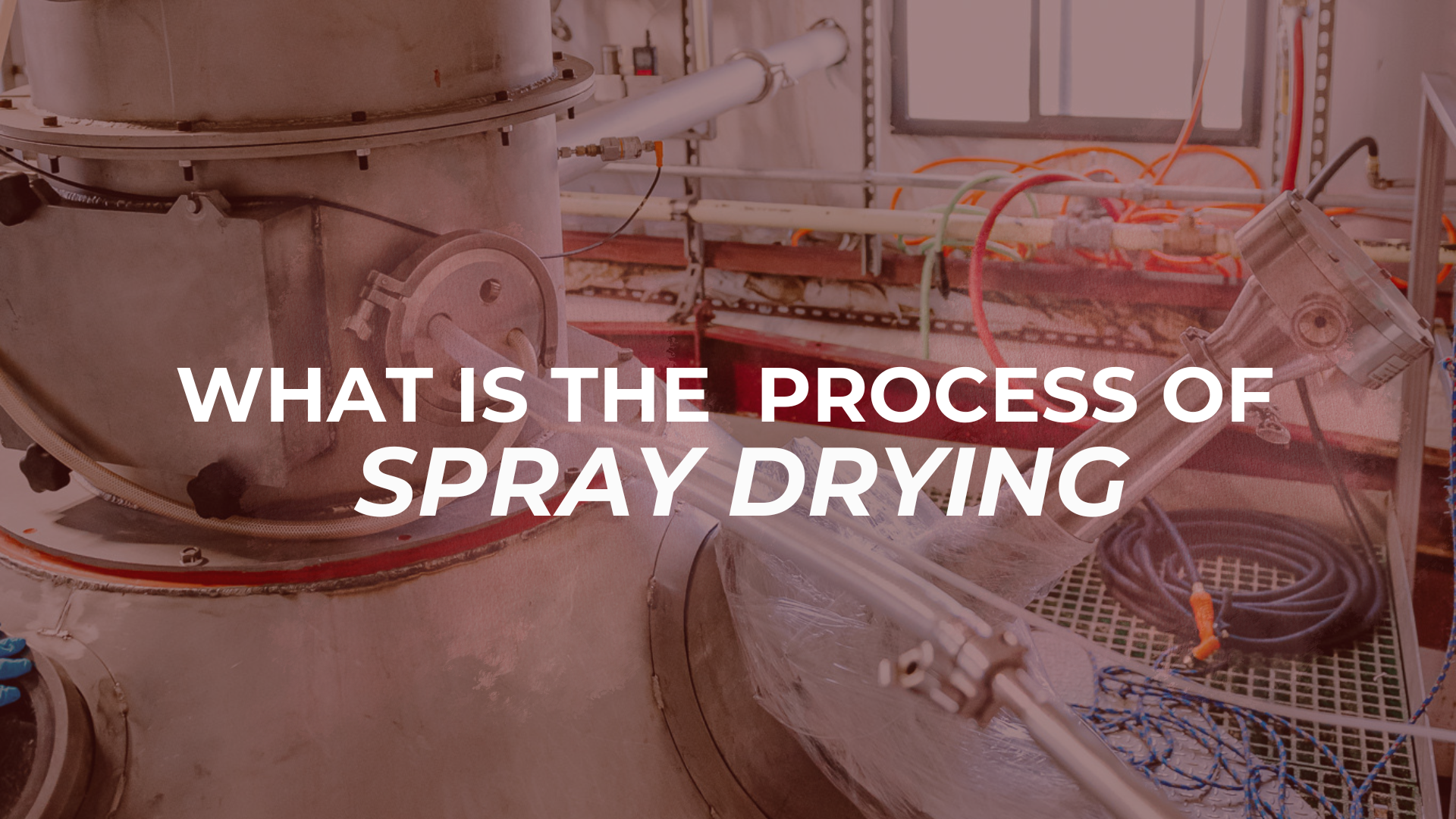 A close-up view of large industrial spray drying machinery with various pipes and equipment. Overlaid white text asks: 'WHAT IS THE PROCESS OF SPRAY DRYING'.